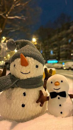 two snowmen standing in the snow wearing hats and scarves