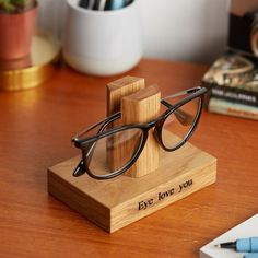 a pair of glasses sitting on top of a wooden stand next to a pen and notebook