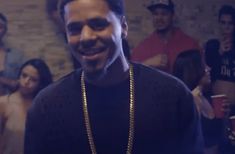 a man wearing a gold chain and smiling at the camera with other people in the background