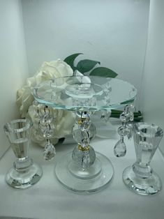 three glass candlesticks sitting on top of a table next to a white rose