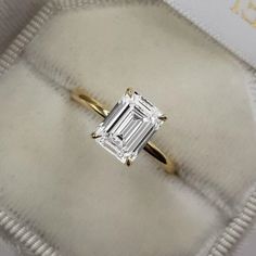 an emerald cut diamond ring sits on top of a cushion