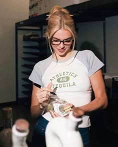 a woman in glasses is pouring something into a teapot and looking at her phone