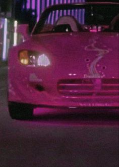 a pink sports car driving down a street at night