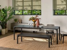 a dining room table with two benches in front of it and potted plants on the side