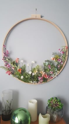 a round wooden frame with flowers and greenery on the wall next to vases