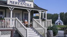 an old fashioned store with flowers on the porch and steps leading up to it's entrance