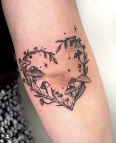 a heart shaped tattoo with mushrooms and leaves on the side of the arm is shown