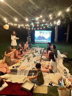 a group of people sitting on top of a grass covered field next to a movie screen