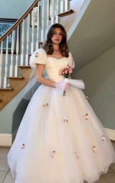 a woman in a white wedding dress standing next to a stair case with flowers on it