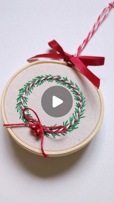 an embroidered christmas ornament with a red ribbon and a video play button on it