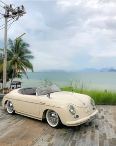 an old style car parked on the side of a road next to some water and palm trees