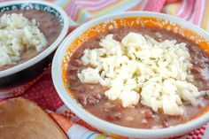 two bowls filled with beans and rice on top of a colorful cloth next to a wooden spoon