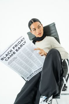 a woman is sitting in a chair reading a newspaper and looking at the camera while holding her leg up