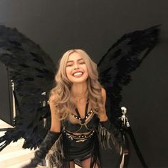 a woman dressed in black and gold posing with wings on her back, smiling at the camera