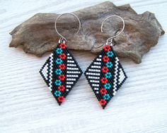 a pair of beaded earrings sitting on top of a piece of wood next to a rock