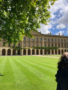 a woman standing in front of a large building on top of a lush green field