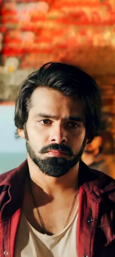 a man with long hair and beard wearing a red shirt is looking at the camera