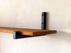 a wooden shelf mounted to the side of a wall with two black brackets on it