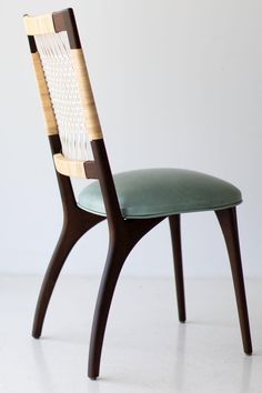 a wooden chair with a green seat and back cushion sitting on a white floor next to a wall