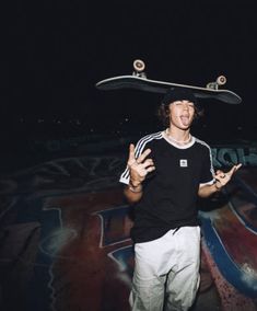 a man standing in front of graffiti holding a skateboard on top of his head