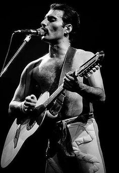 a shirtless man holding a guitar and singing into a microphone