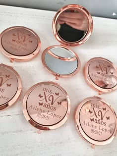 six personalized compact mirrors on top of a white table with a person's hand in the mirror