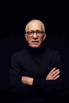 an older man with glasses is posing for a photo in front of a black background