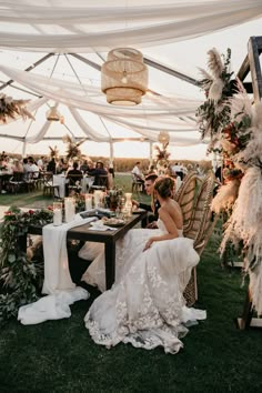 a woman sitting at a table in front of a white tent with flowers and greenery