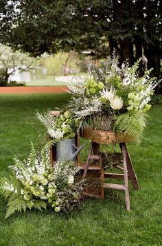 an arrangement of flowers and greenery is arranged on the grass in front of a wooden stand