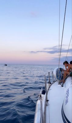 two people sitting on the bow of a sailboat in the middle of the ocean