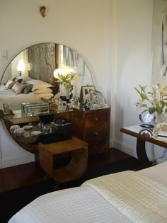 a mirror sitting on top of a wooden dresser next to a white bed in a bedroom