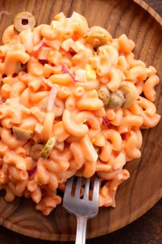 a wooden plate filled with macaroni and cheese on top of a table next to a fork