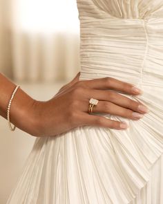 a woman in a white dress holding onto her wedding band and wearing a gold ring