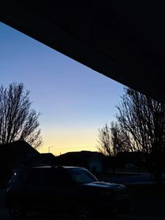 two cars parked in a parking lot at dusk with the sun going down behind them