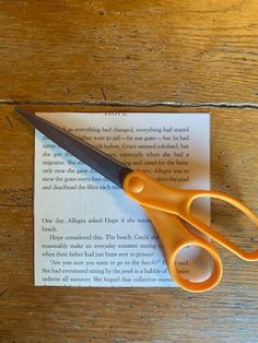 an orange pair of scissors sitting on top of a piece of paper next to a book