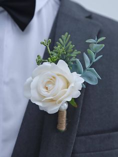 a boutonniere with white flowers and greenery on the lapel of a man in a tuxedo