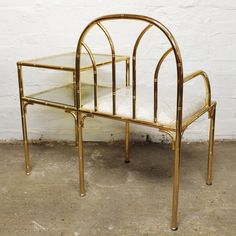 a gold metal and glass side table against a white brick wall