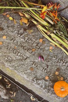 a memorial stone with writing on it and flowers in the foreground, surrounded by small orange pumpkins