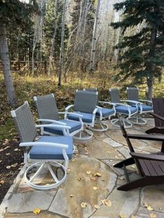 several lawn chairs are lined up on a stone walkway in the woods with trees behind them