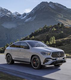 a silver mercedes suv driving down a road with mountains in the background