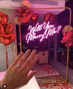 a woman's hand with pink nail polish holding up a ring in front of a neon sign