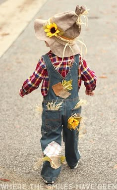 a little boy walking down the street wearing overalls and a hat with sunflowers on it