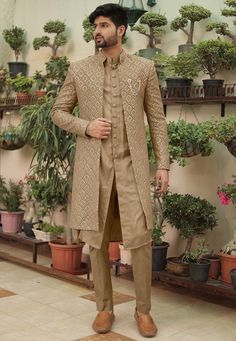 a man standing in front of potted plants wearing a tan sherve and brown pants