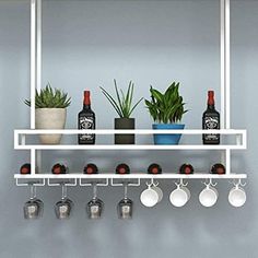 a white shelf with cups and mugs on it next to a potted plant