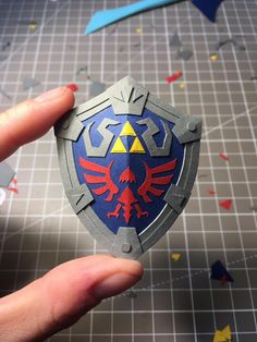 someone is holding up a paper model of the legend of zelda shield with red, yellow and blue colors