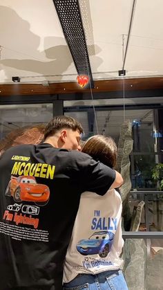 two people are hugging each other in front of a glass window with cars on it