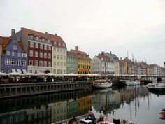 people are sitting on boats in the water near some buildings and docked sailboats with umbrellas over them