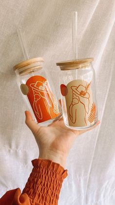 someone holding two cups in their hand with designs on them, one is orange and the other is white