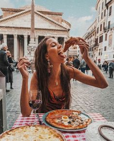 a woman sitting at a table eating pizza and drinking wine