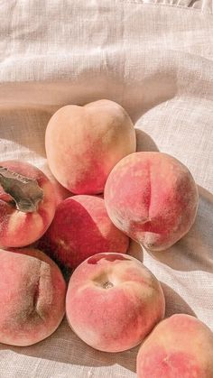 several peaches are sitting on top of a linen covered tablecloth with a leaf sticking out of it